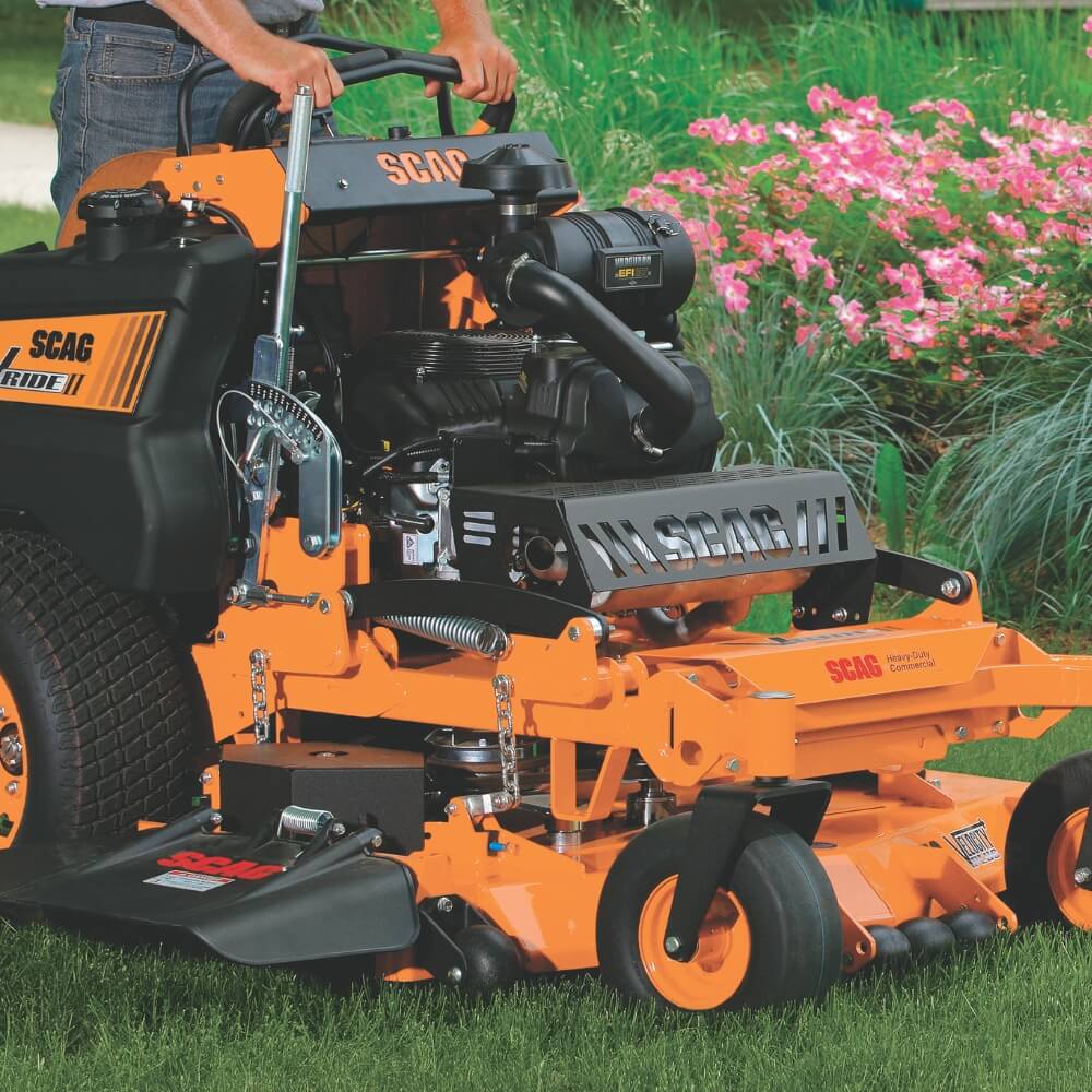 Orange SCAG riding lawn mower on grass with flowers in the background