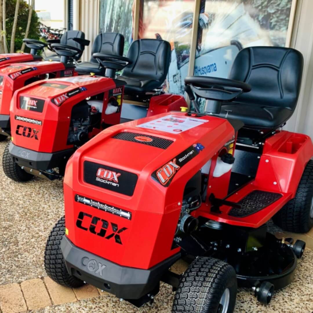 Red Cox riding lawn mowers on display outside a building.