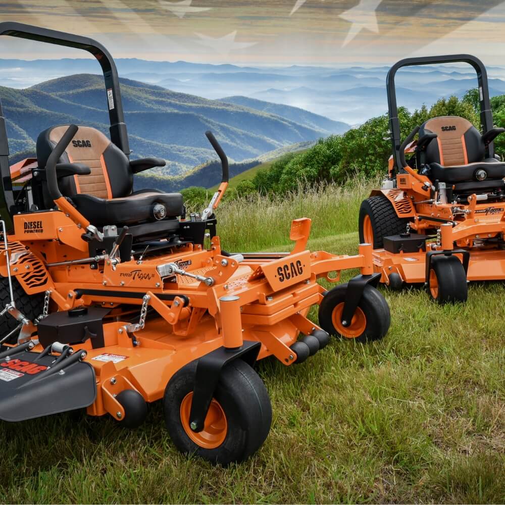 Two orange SCAG zero-turn mowers on a grassy field with a scenic background.